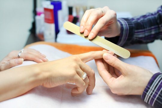 Manicurist hands make manicure by nailfile for woman in salon