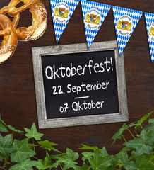 Tafel mit Oktoberfest auf Holz mit Efeu, Bretzel und Wimpeln