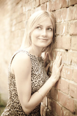 Fototapeta premium Cute blonde lady standing near a brick wall