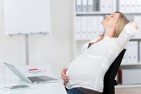 glückliche schwangere frau im büro streckt sich