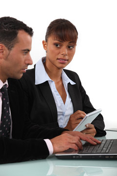 Woman taking notes as a businessman uses a computer