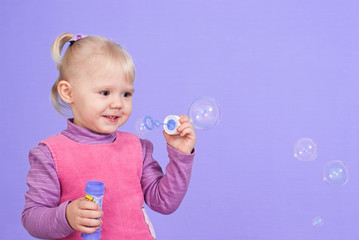 A small charming good Caucasian girl plays with bubbles