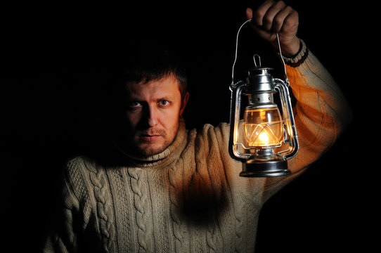 Man in the night with a burning kerosene lamp on black