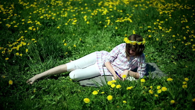 Teenager girl lying on meadow full of sow-thistle and writing