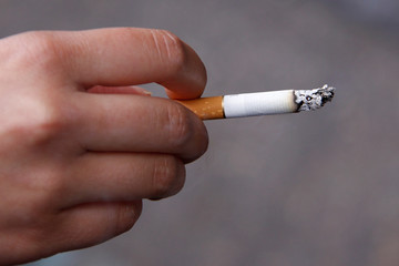 hand holding unbranded cigarette against grey pavement background 