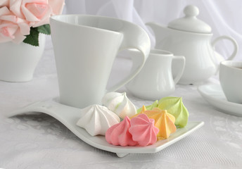 Meringue cookies of different colors on a plate with a cup of co