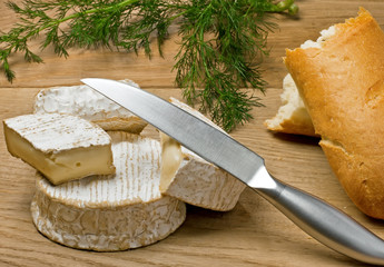 Brie and Camembert cheeses, bread and dill on the table