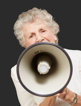 portrait of senior woman screaming with megaphone over black bac