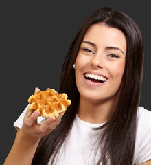 portrait of young woman holding waffle over black background
