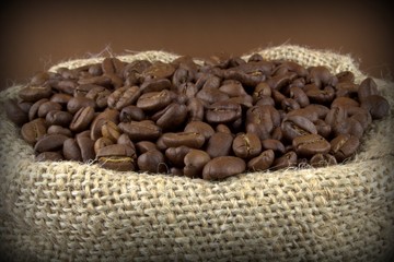 Coffee beans in a flax sack on brown background