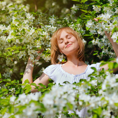Young blonde woman with the apple tree on a warm summer day