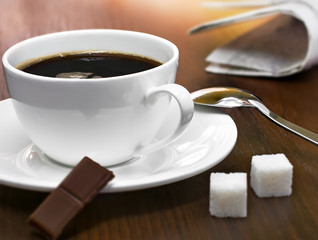 Coffee cup, sugar cubes, chocolate and newspapers on a table