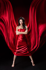 Mysterious  woman in red waving silk dress over black background