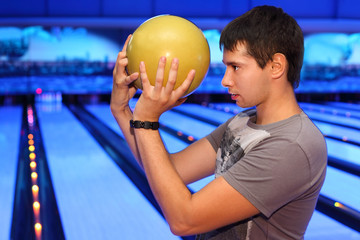 Young man holds yellow ball and prepares to throw in bowling