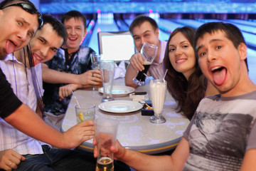 Friends sit at table and drink beer and cocktails in bowling