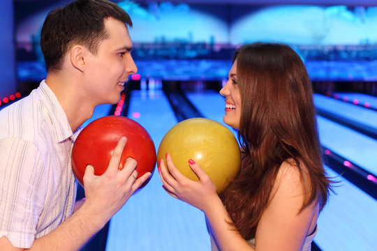 Happy man and woman hold balls and look at each other in bowling