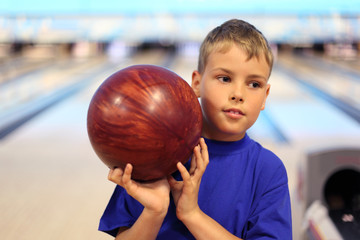 Fototapeta premium thinking boy dressed in T-shirt holds ball in bowling club