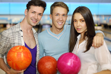 Two young men and beautiful girl hold balls in bowling club