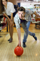 Young smiling man wearing ripped jeans throws ball in bowling;