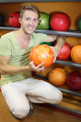 Fototapeta premium Young smiling man sits near shelves with balls and holds ball