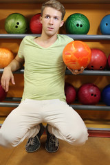 Fototapeta premium Young pensive man sits near shelves with balls