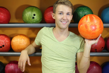 Fototapeta premium Happy man stands near shelves with balls and holds orange ball