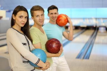 Two happy men and girl smile and hold balls in bowling club;