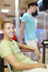 Young man sits at table and smiles; other man stands