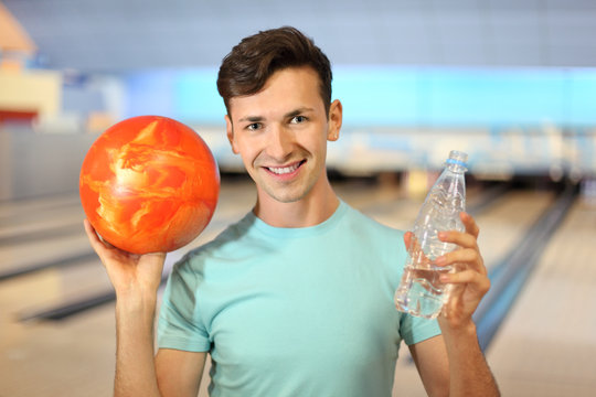 Young Man Holds Ball And Bottle With Water In Bowling Club