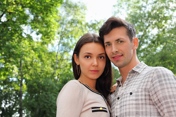 Obraz premium Beautiful man and woman stand in park; green trees and sunny day