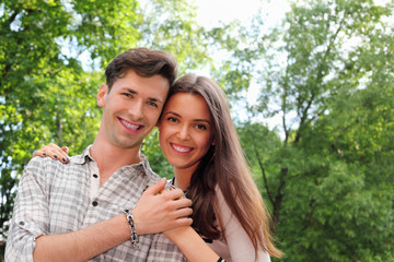 Smiling young man and woman stand in park and hold hands