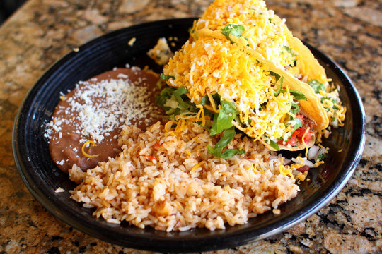 Delicious Crunchy Tacos With Beans And Rice At A Restaurant.