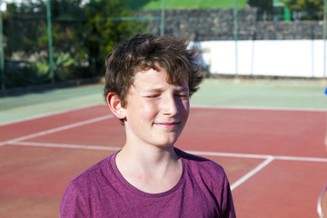 smart smiling boy  at the outdoor tennis court with closed eyes