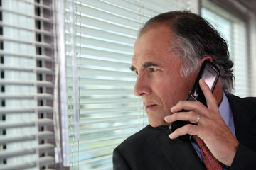 Senior businessman looking through blinds whilst making call