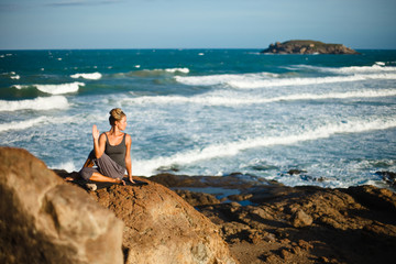 Young woman doing yoga on a rocky seashore