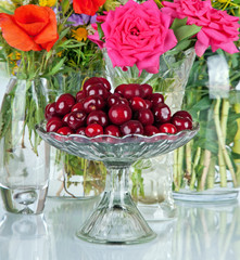 fresh red cherries in a beautiful glass bowl and many flowers