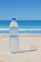 A bottle of cool water on the beach near the sea.