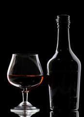 Glass of brandy and bottle on black background