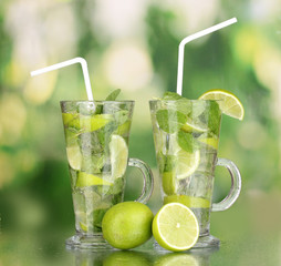 Glasses of cocktail with lime and mint on green background