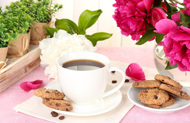 cup of coffee, cookies and flowers on table in cafe