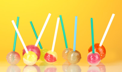 Bright and delicious lollipops on yellow background close-up