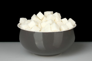 White lump sugar in bowl on black background
