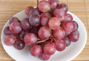 Red grape branch on white round plate