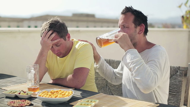 Young man comforting his sad, depressed friend in bar