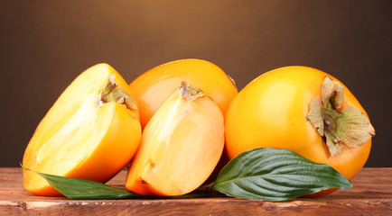 Appetizing persimmons on wooden table on brown background