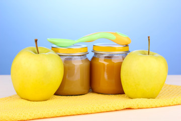 Jars of baby puree on napkin on blue background