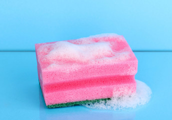 Sponge with foam of dishwashing liquid on blue background