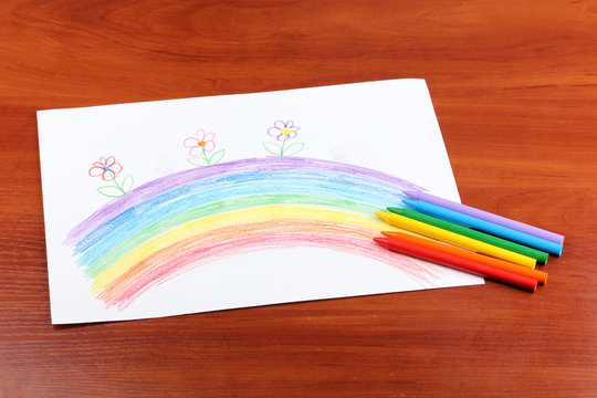 Children's drawing of rainbow and pencils on wooden background