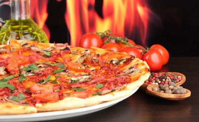 delicious pizza and tomatoes on wooden table on flame background