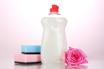 Dishwashing liquid with sponges and flower on pink background